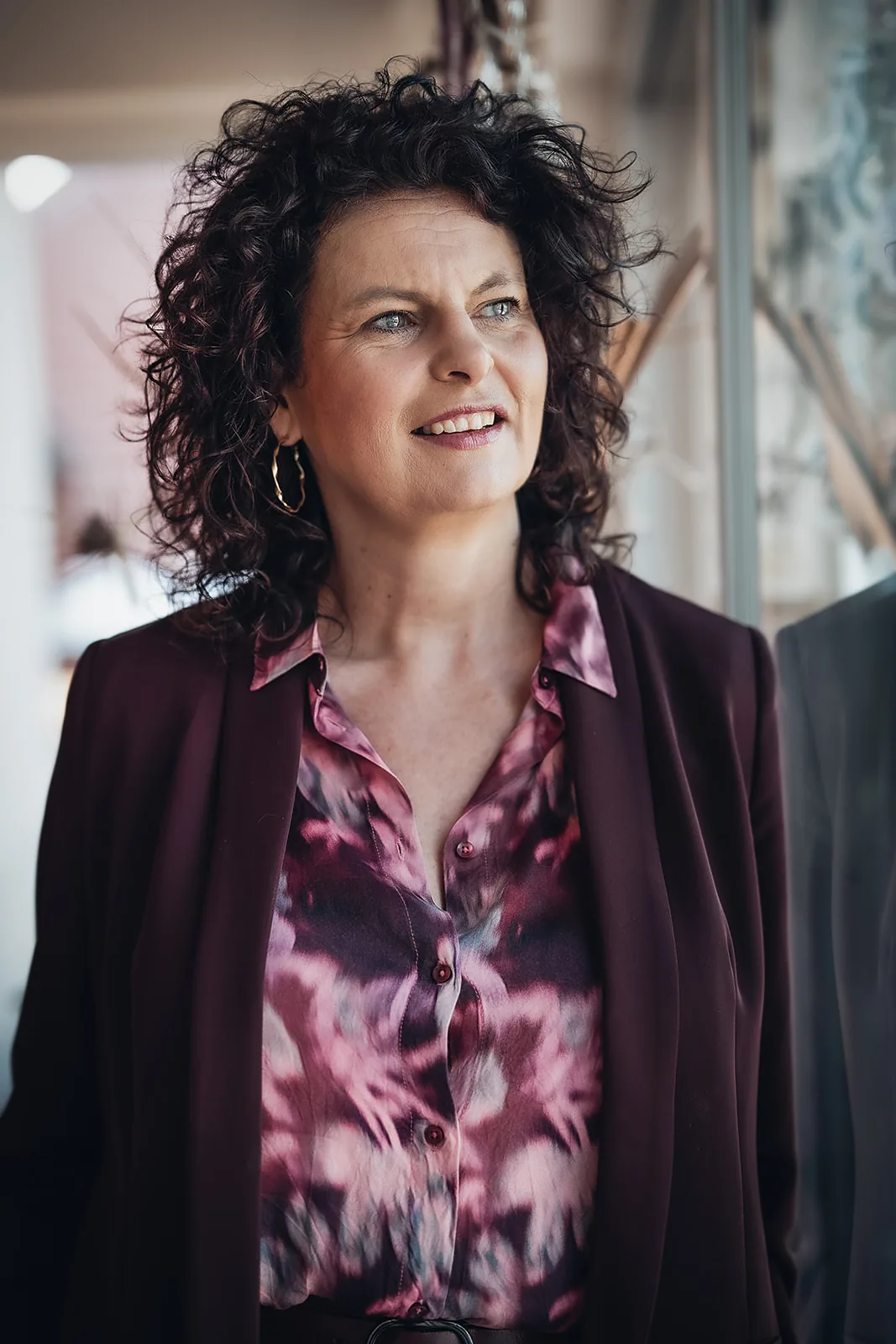 Martina Koch-Lang steht am Fenster in dunklem Blazer und blickt lächelnd zur Seite.